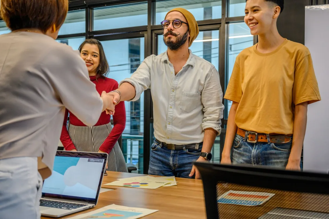 A young team welcoming a new hire with a handshake over laptops and charts