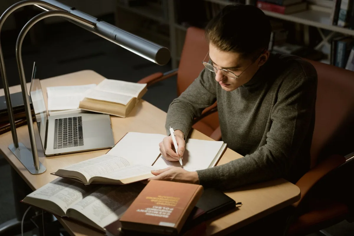 Man taking handwritten notes while studying from a book
