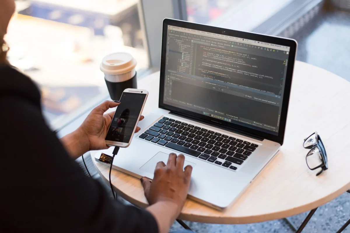 Person holding a smartphone while working on a laptop
