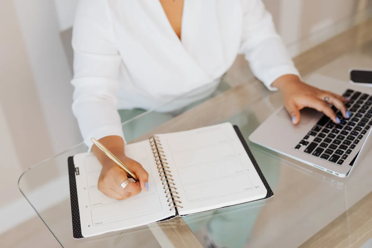 Freelancer writing tasks in a notebook next to a laptop