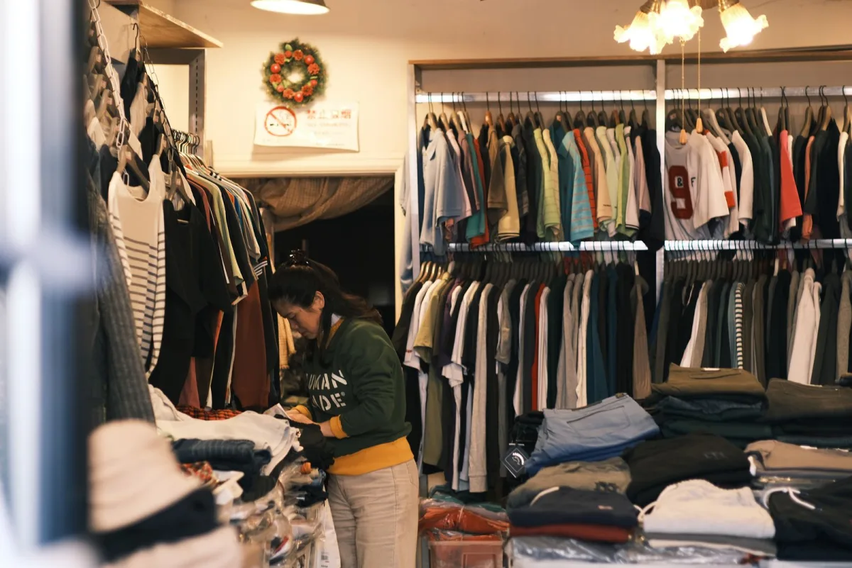 Shop owner sorting garments between racks in a small clothing store