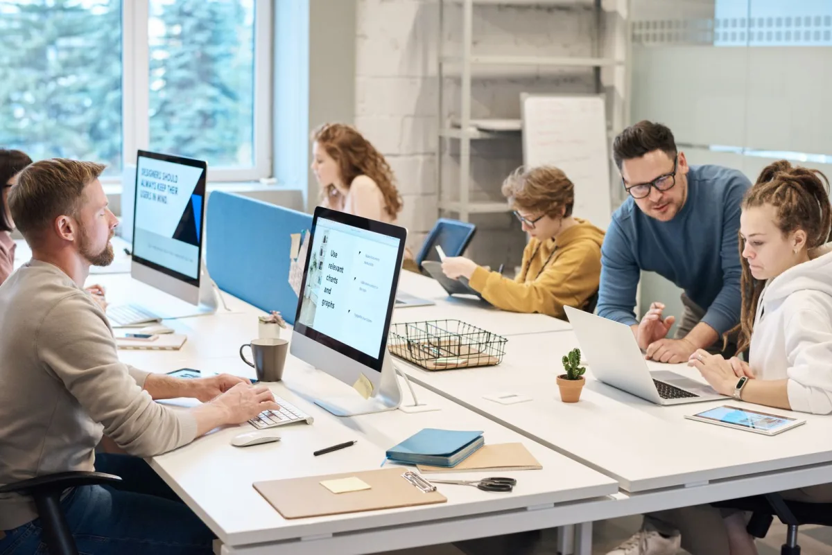 Mitarbeitende eines kleinen Unternehmens arbeiten an Bildschirmen im Büro