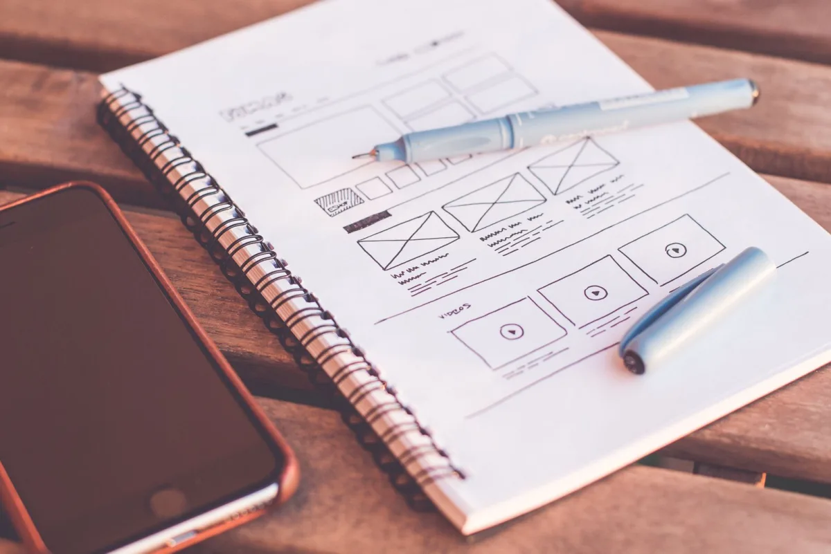 Hand-drawn app wireframes in a notebook next to a smartphone