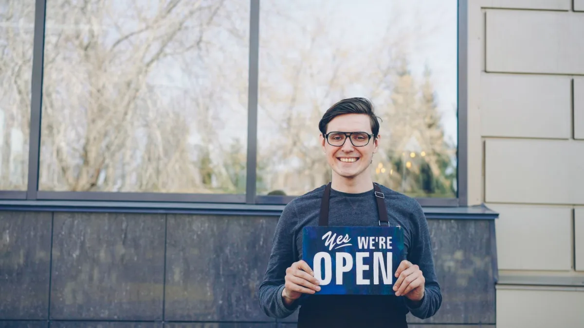 Lächelnde Ladenbesitzerin hält ein Open-Schild vor ihrem Geschäft