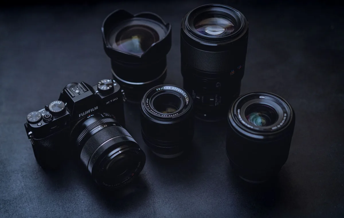 Camera body with several lenses laid out on a dark table