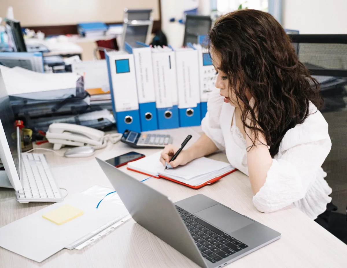 Freelance writer taking notes in a notebook next to her laptop