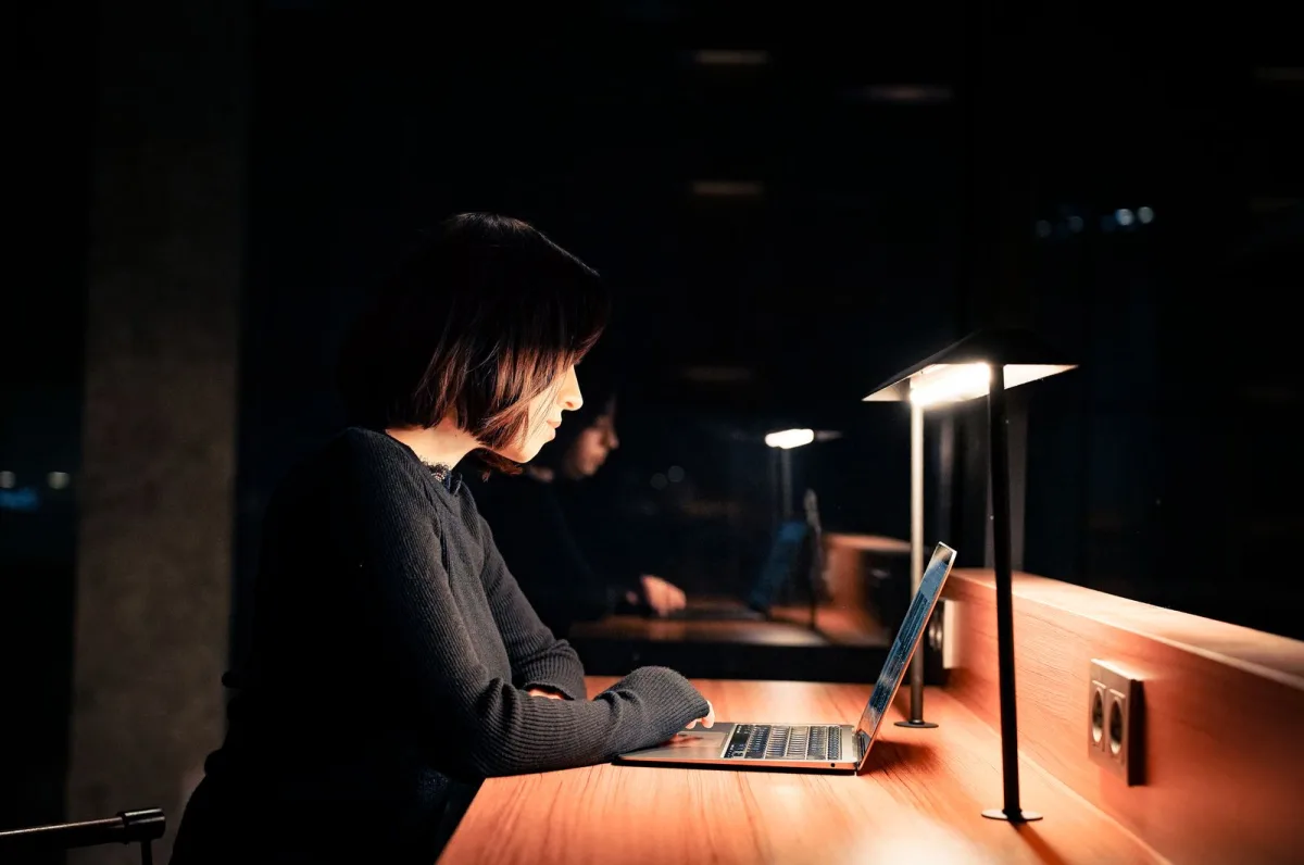 Frau arbeitet abends im Schein einer Schreibtischlampe am Laptop