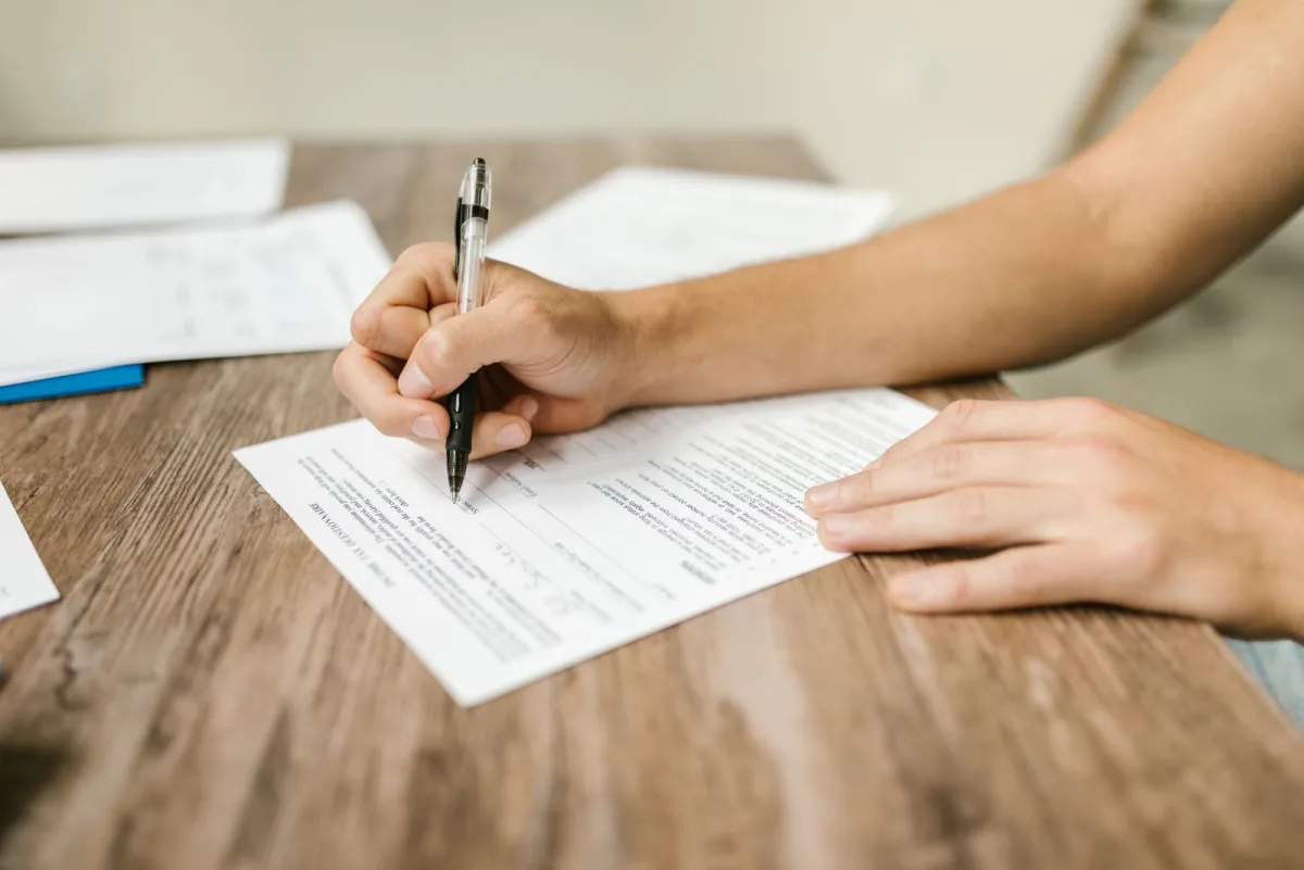 Nahaufnahme einer Hand, die ein Formular mit dem Stift ausfüllt